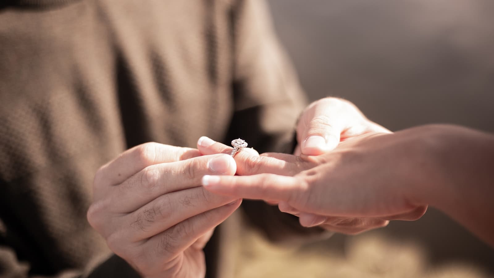 A diamond ring held between two fingers in daylight